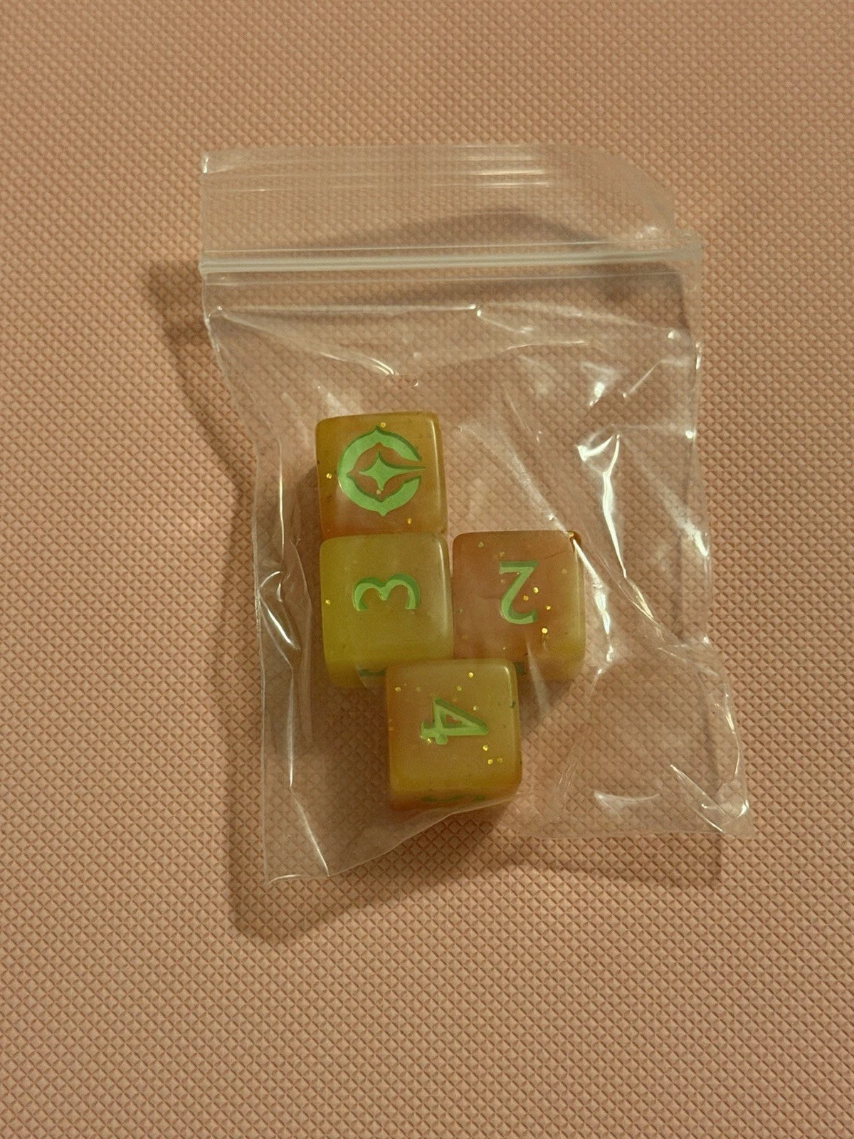 Set of four dice with green numbers on a clear plastic bag against a beige background